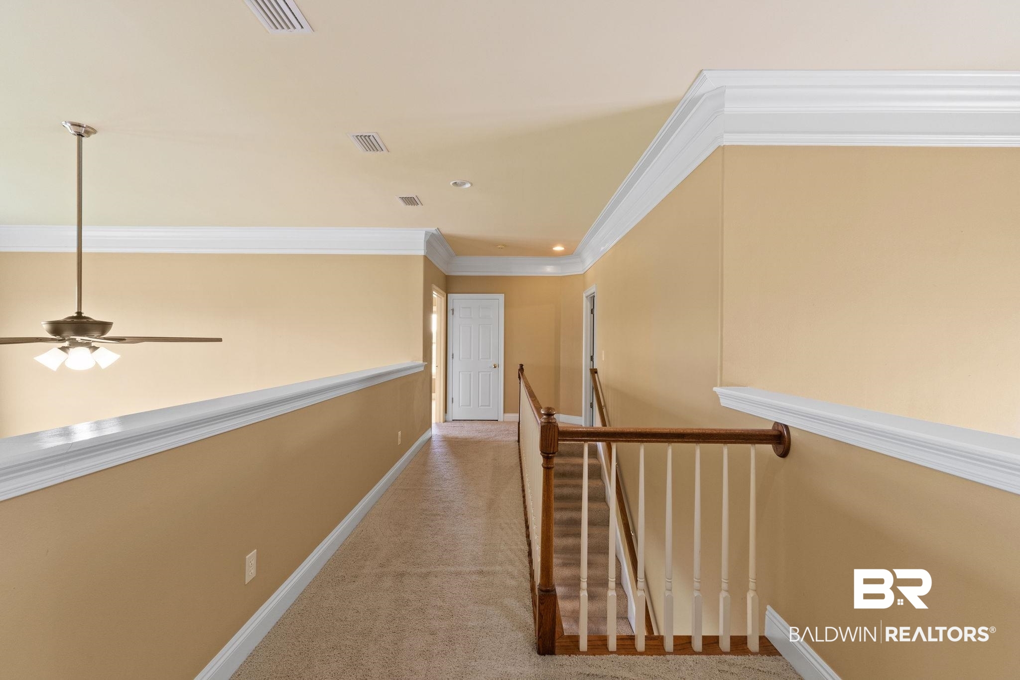 Upstairs hallway with beige walls, carpet, white trim, and a wood-and-white stair railing.