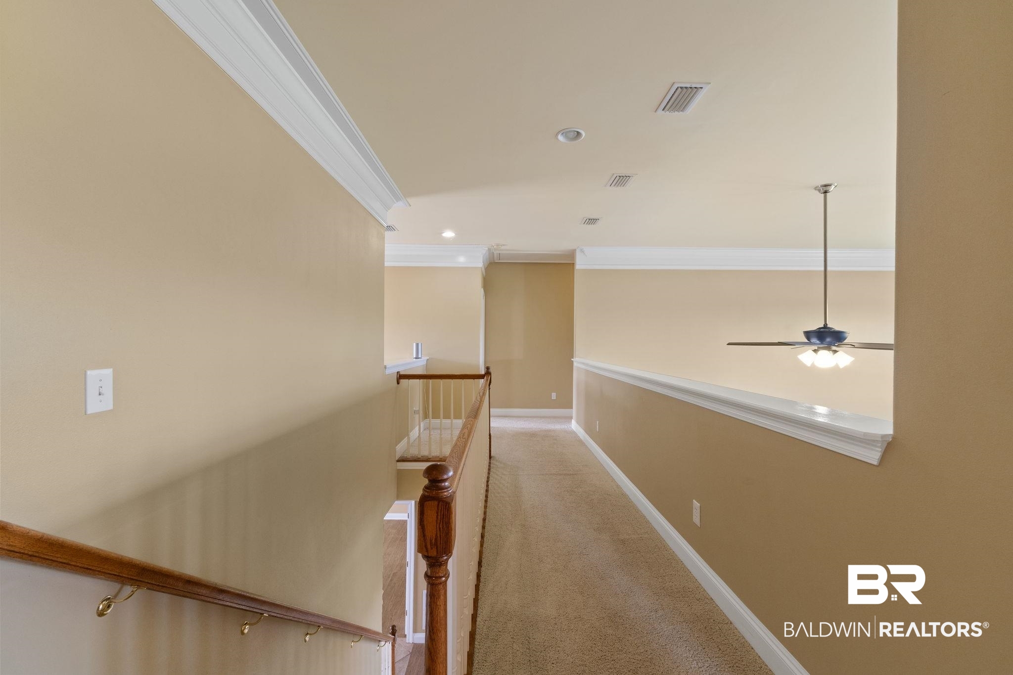 Carpeted upstairs hallway with beige walls, white trim, and a wooden stair railing.