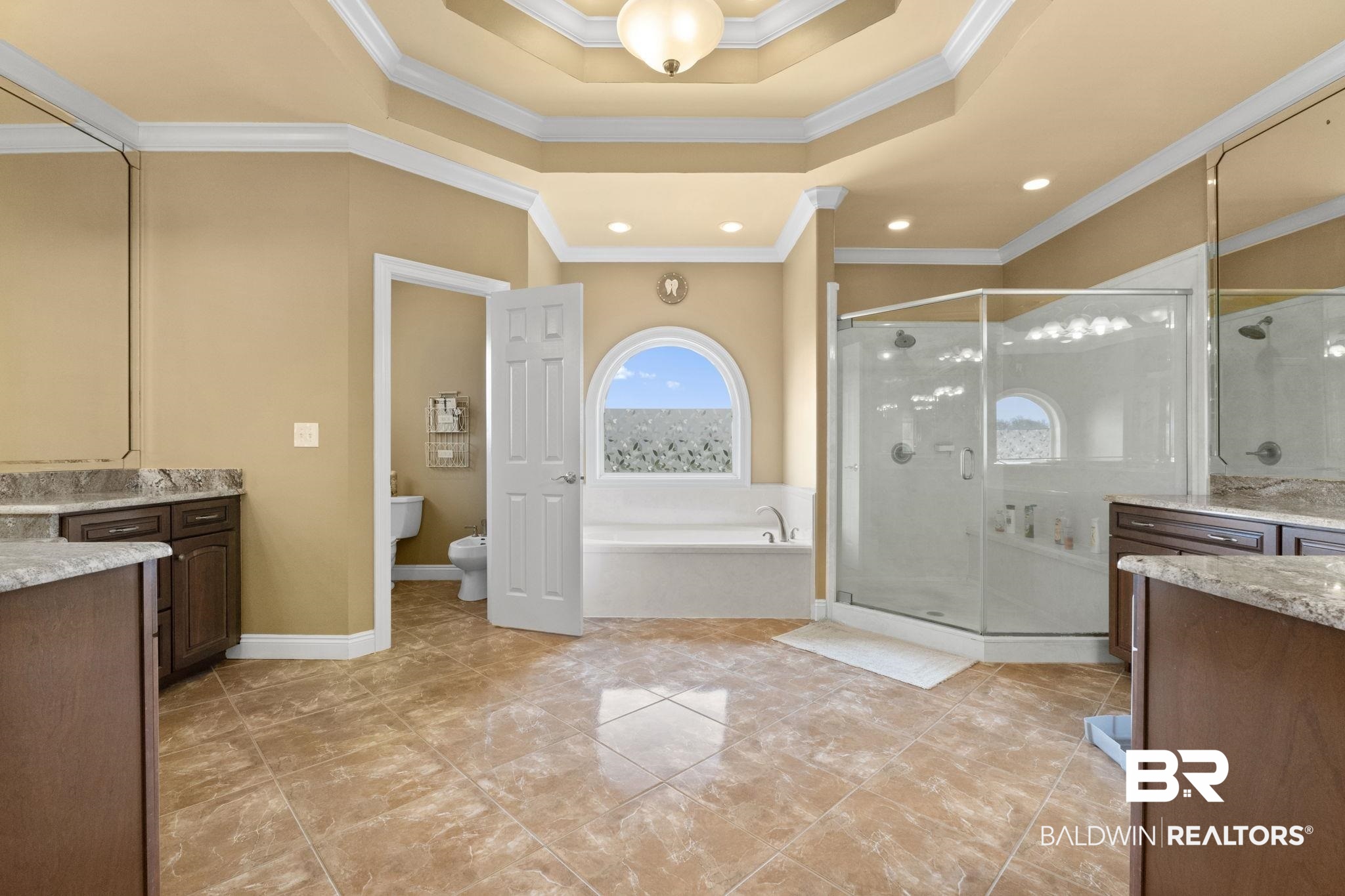 Spacious bathroom with a glass shower, built-in tub beneath an arched window, and double vanity.
