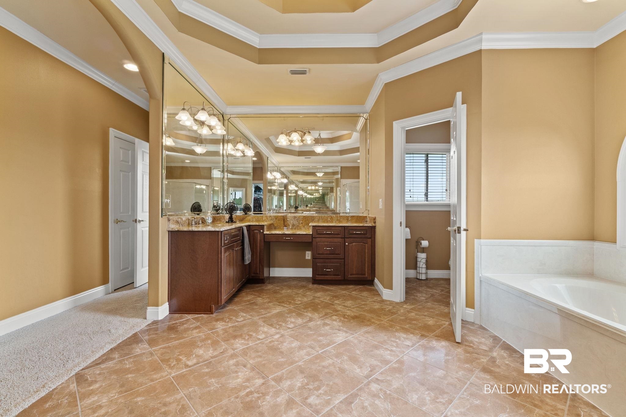 Primary bathroom with a dark wood double vanity, expansive mirrors, and a built-in soaking tub.