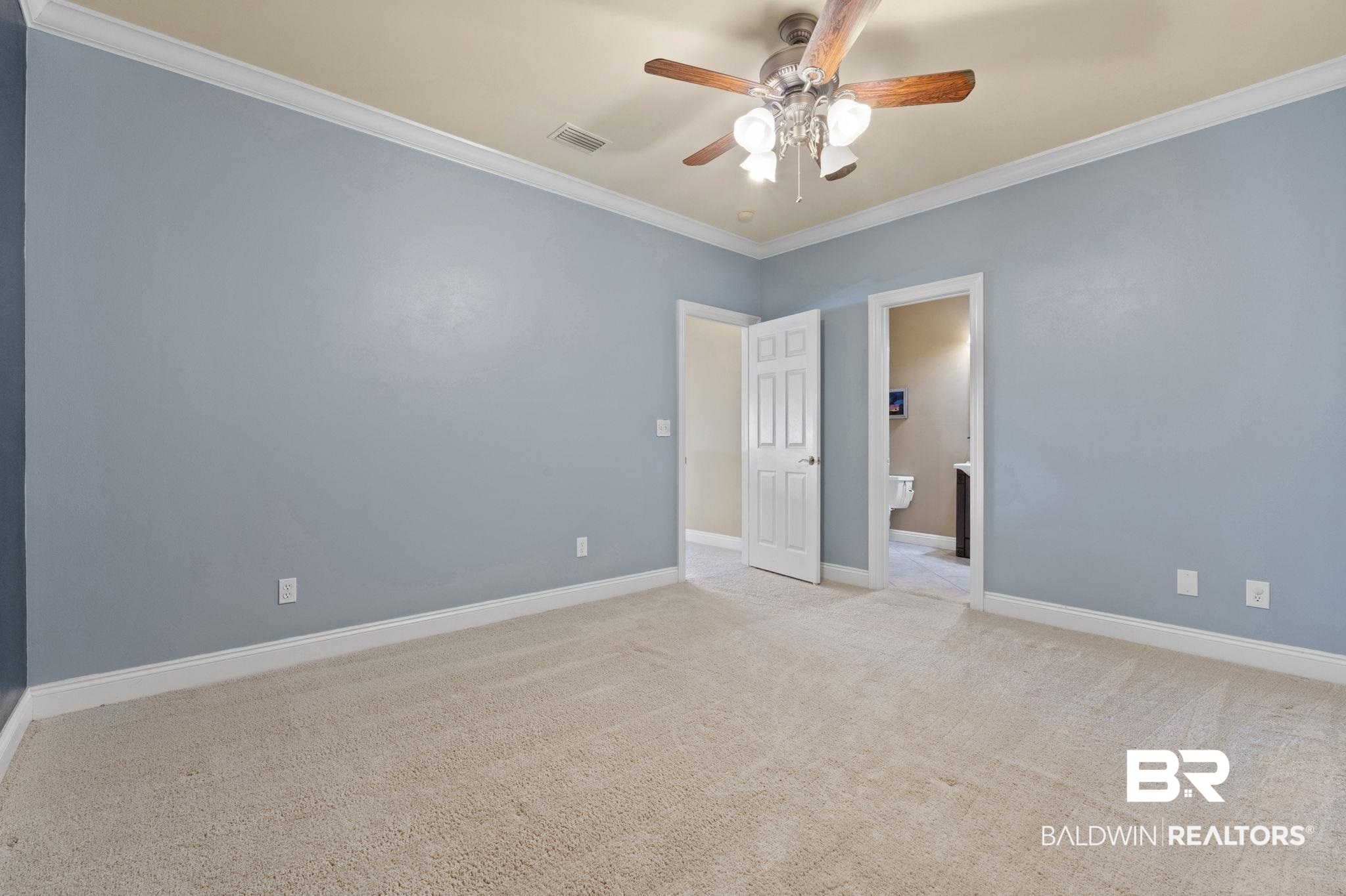 Empty bedroom with blue walls, beige carpet, and a ceiling fan; open doorways lead to adjoining rooms.