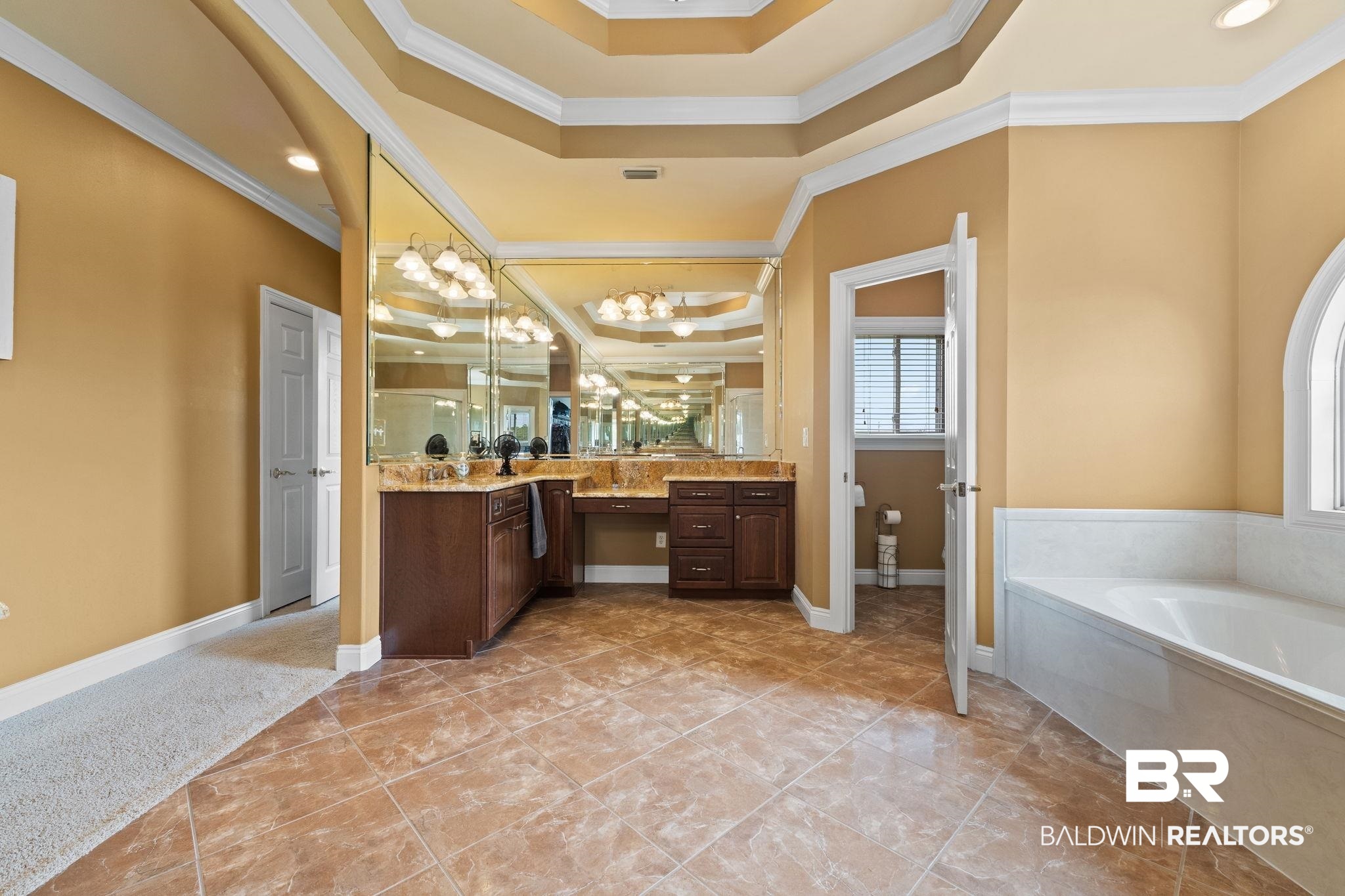 Bathroom with mirrored dark wood vanity, granite counter, tray ceiling, and white soaking tub.