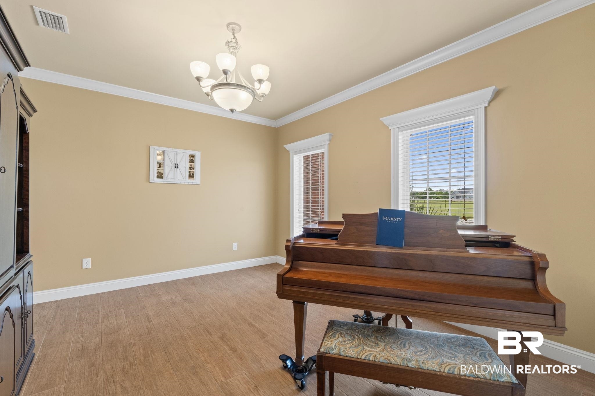 Music room with a polished grand piano and patterned bench beside two windows.