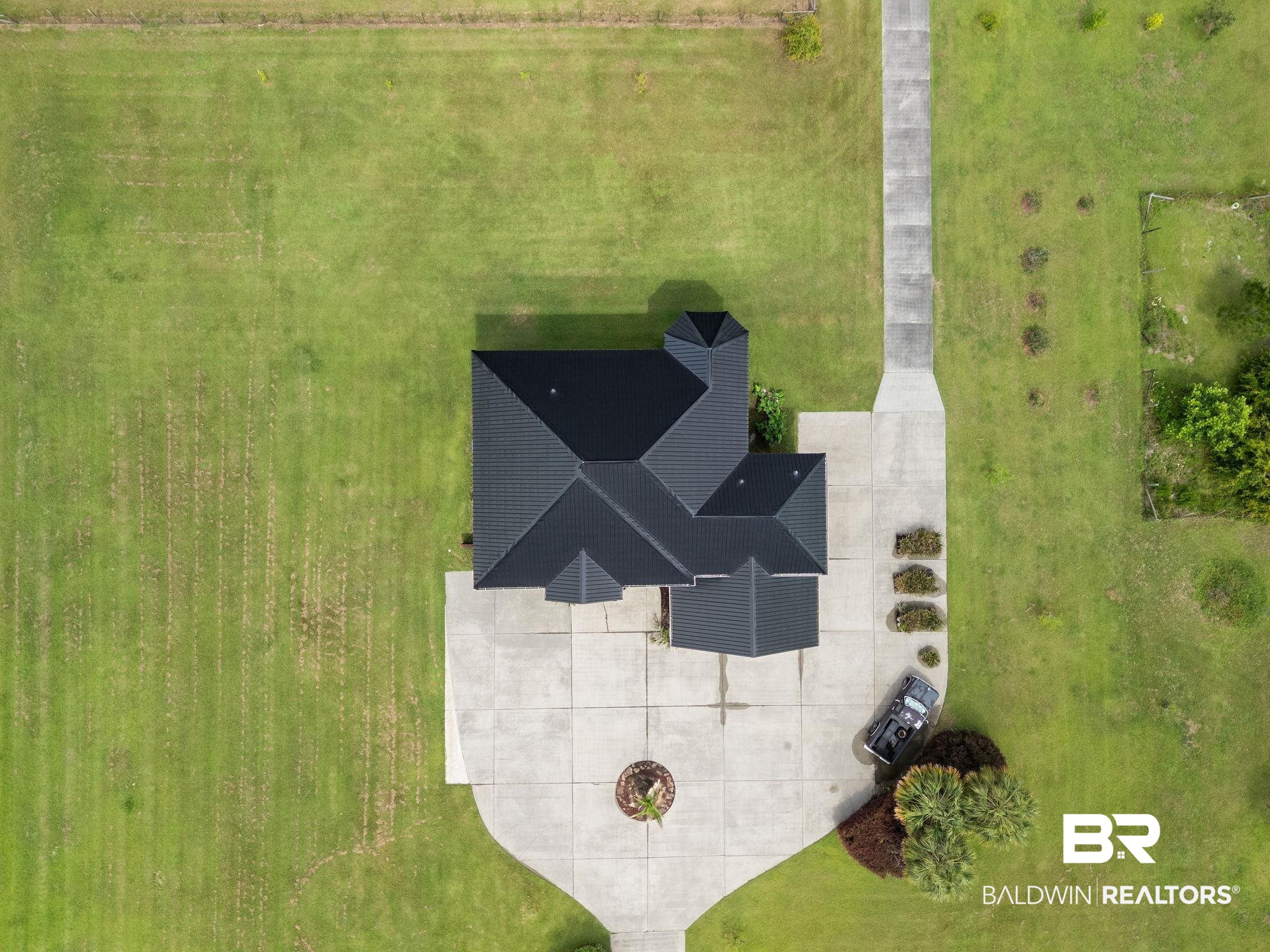 Aerial view of a home with a dark roof, broad concrete driveway, and expansive lawn.