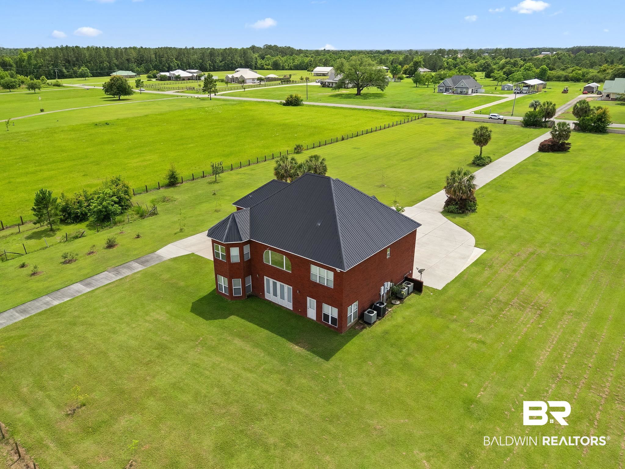 Aerial view of a two-story brick house with a dark roof, broad lawn, and curving concrete driveway.