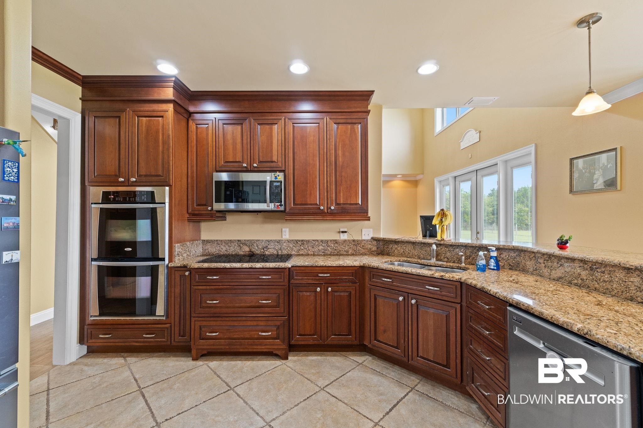 Kitchen with dark cherry cabinets, granite counters, double wall oven, and windows overlooking the yard.