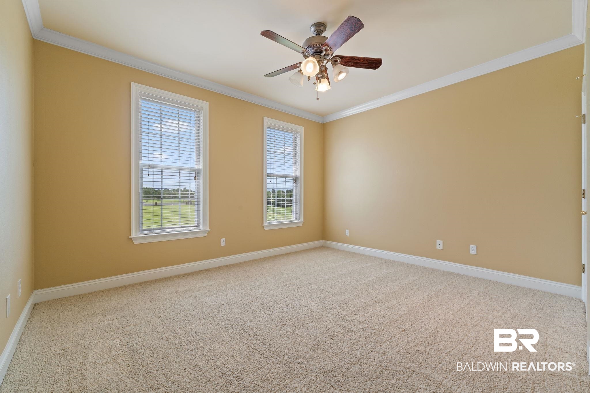 Empty beige bedroom with carpet, two blinded windows, and a ceiling fan.