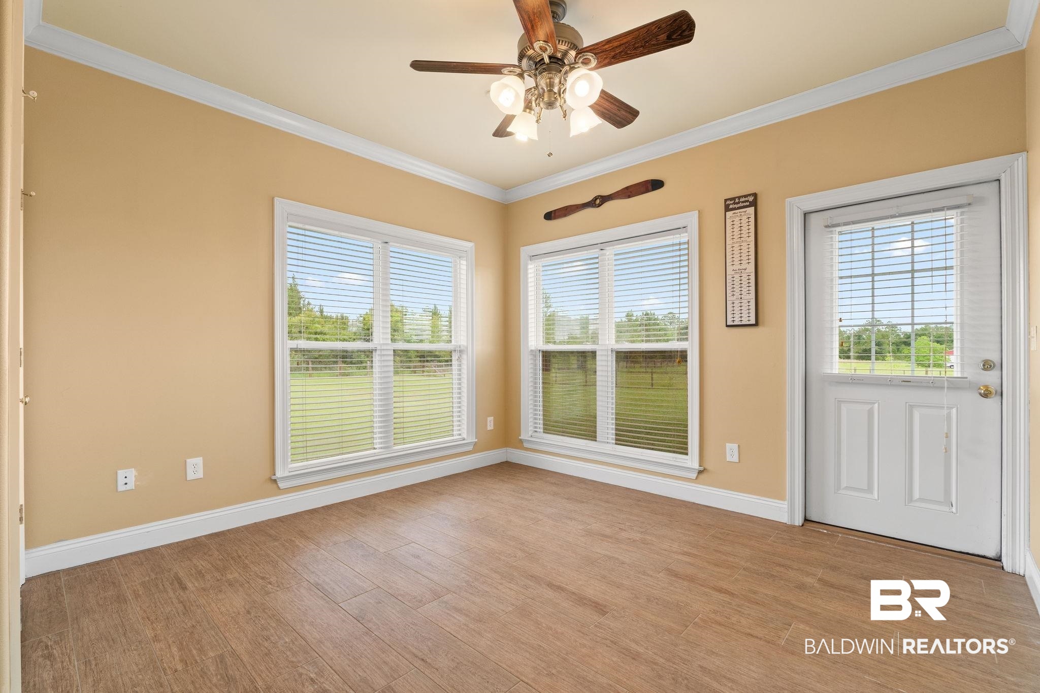 Empty room with brown tile flooring, three windows, a white exterior door, and a ceiling fan.