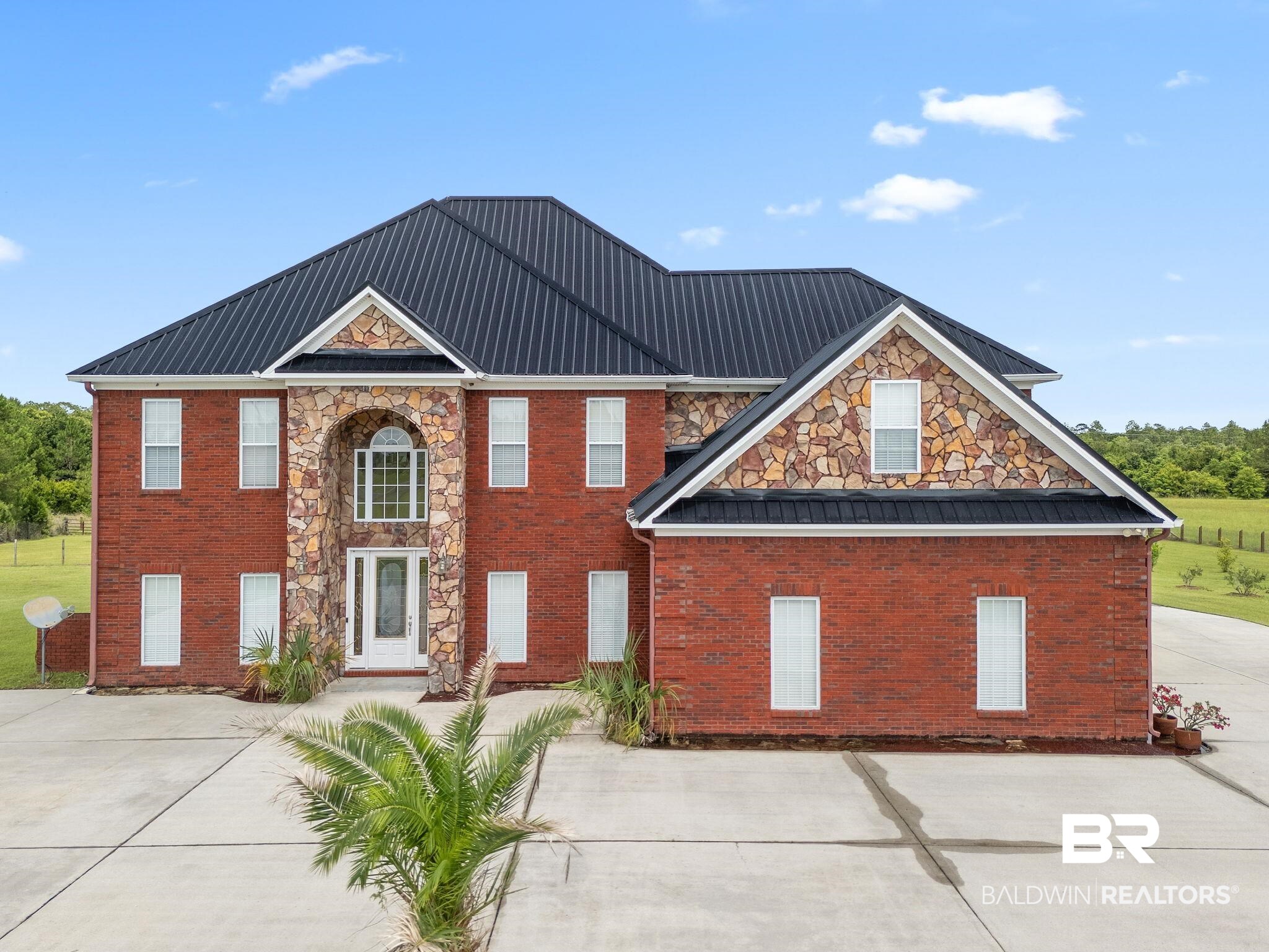 Two-story red-brick house with stone entry, dark metal roof, and broad concrete driveway.