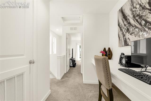 Home office with a computer desk and upholstered chair beside a carpeted hallway.