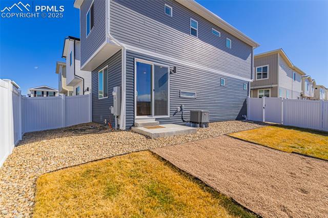 Rear of a gray two-story home with a sliding door, white fencing, gravel landscaping, and a concrete walkway.