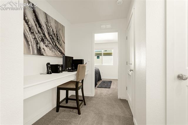 Office nook with a white desk and computer beside a hallway leading to a bedroom.