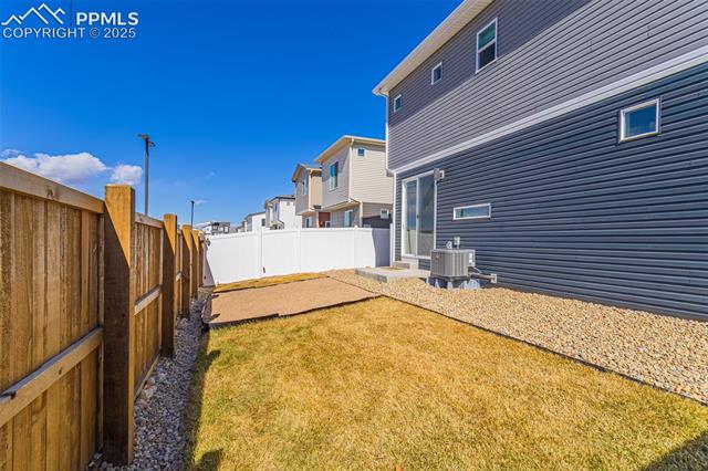 Fenced backyard with a patchy lawn, gravel border, and gray-sided house.