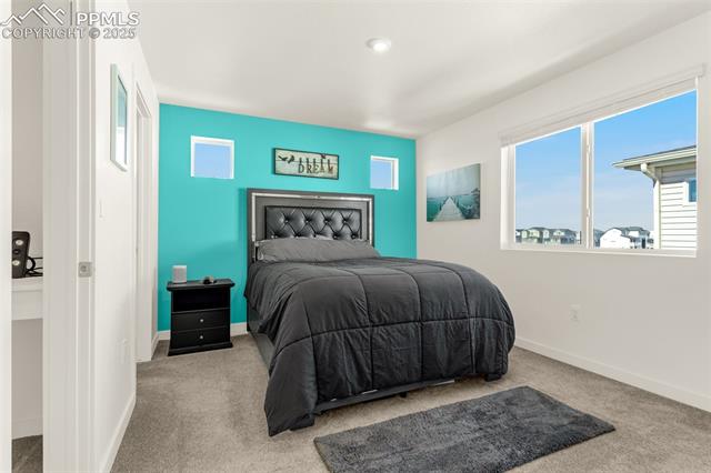 Bedroom with a black tufted bed, turquoise accent wall, and large windows overlooking neighboring homes.