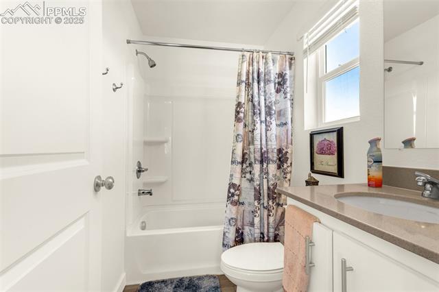 Bathroom with a patterned shower curtain, white tub and toilet, and beige vanity beneath a window.
