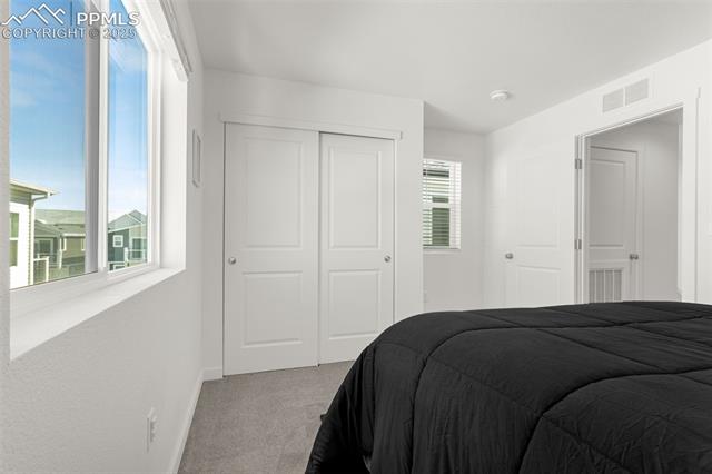 Bedroom with a black quilted bed, sliding closet doors, and a window overlooking neighboring homes.