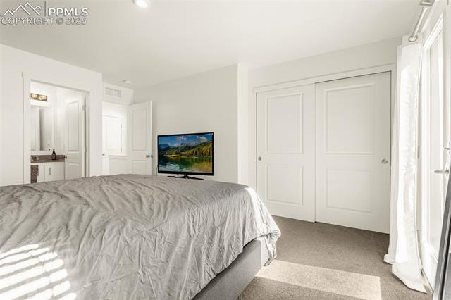 Bedroom with a gray-quilted bed, white closet doors, and sunlight through a glass door.