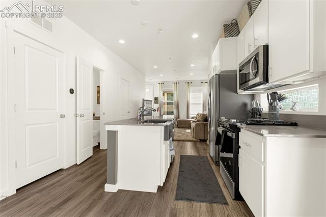 Bright white kitchen with a central island, stainless steel appliances, and wood-look flooring.