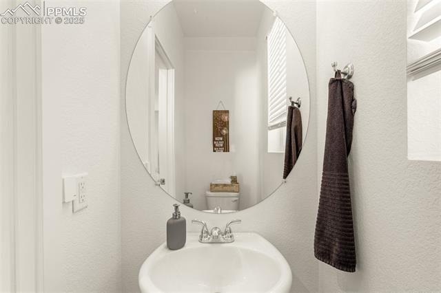 Bathroom sink with a chrome faucet, round mirror, and dark hand towel.
