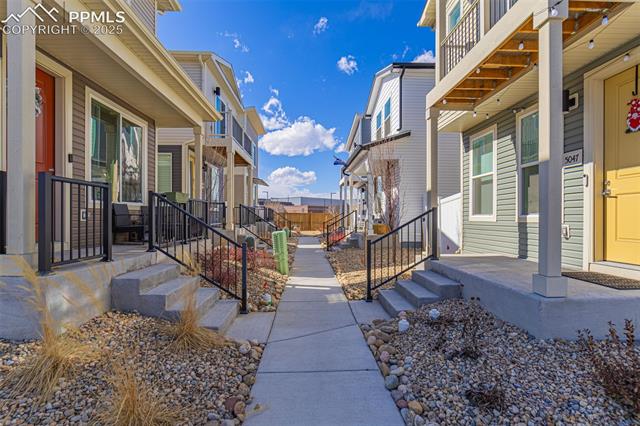 Shared walkway between modern townhomes with porches and gravel landscaping.