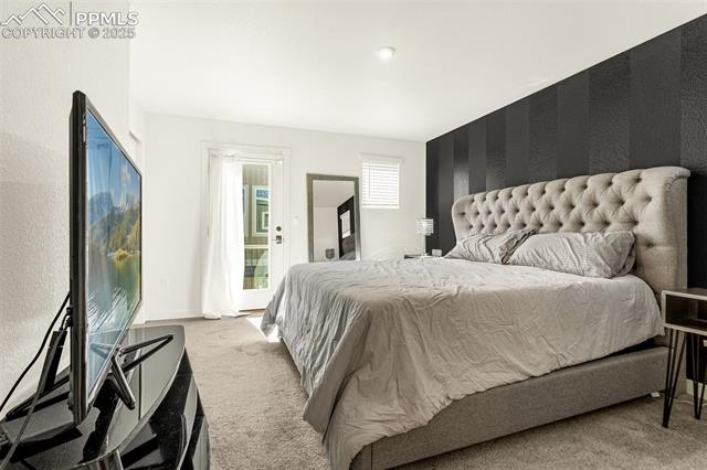 Staged bedroom with a tufted upholstered bed, dark striped accent wall, and television.