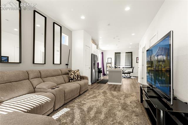 Open-plan living room with a beige sectional, large rug, and television facing the kitchen island.
