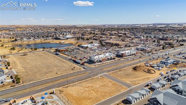 Aerial view of a neighborhood with vacant lots, commercial buildings, and a small pond.