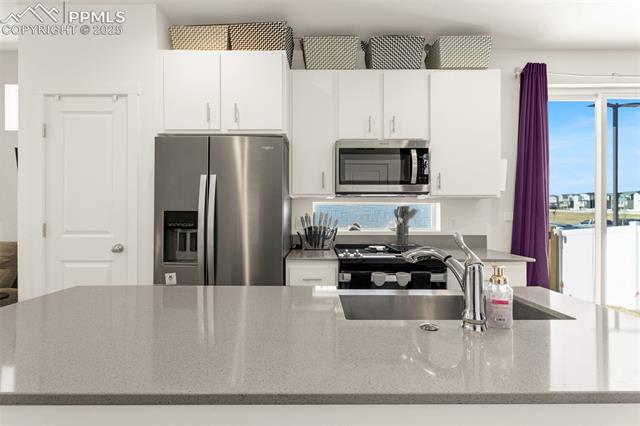 Modern kitchen with white cabinets, stainless-steel appliances, and a large stone island.
