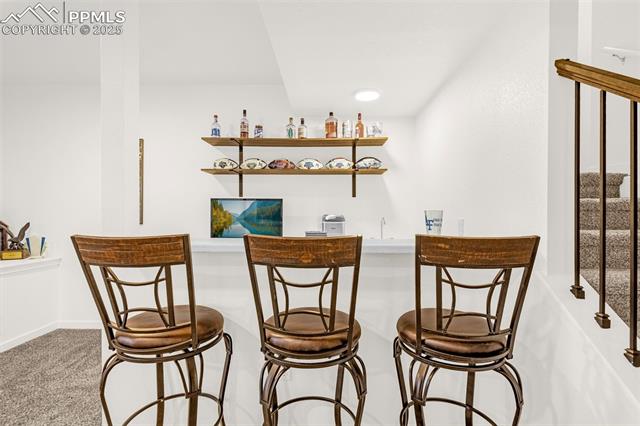 Basement bar with three wooden stools and wall-mounted shelves holding bottles and dishes.