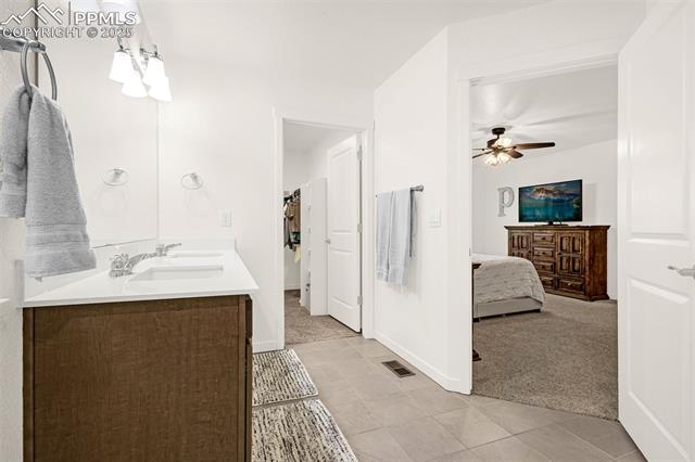 Bathroom with a wood vanity and tiled floor, opening into a furnished bedroom.