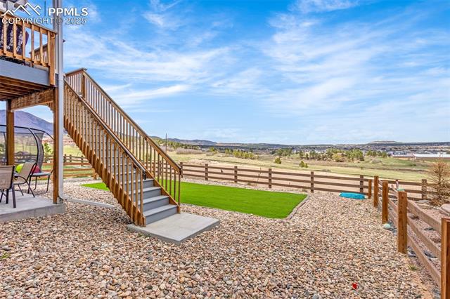 Backyard with wooden deck stairs, gravel landscaping, a small green lawn, and open views toward distant hills.