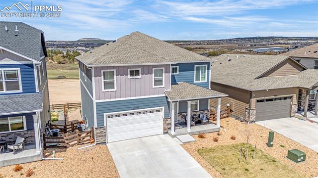 Aerial view of a two-story blue-gray home with an attached garage and covered porch, neighboring homes and distant hills.