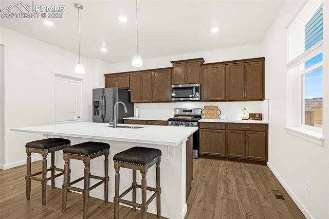 Kitchen with dark wood cabinets, stainless steel appliances, and a white island with three bar stools.