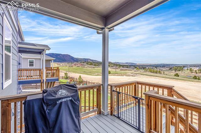 Covered wooden deck overlooking open land and distant mountains, with a covered grill in the foreground.