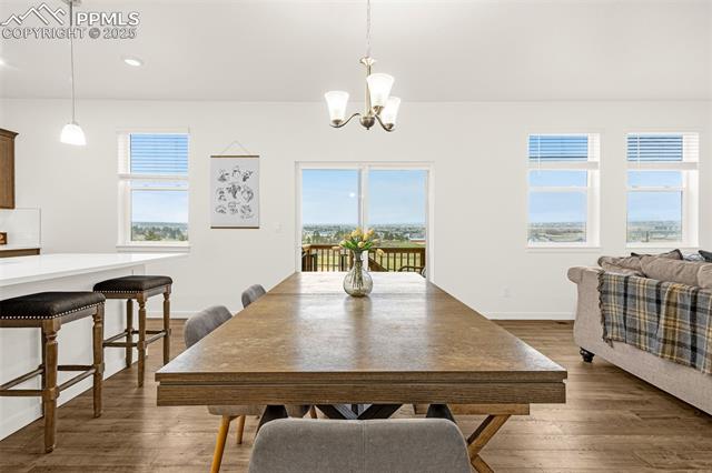 Dining area with a long wooden table, bar stools, and large windows overlooking a distant landscape.