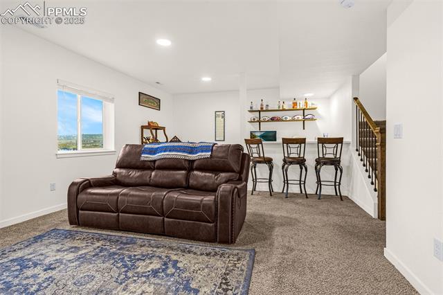 Living room with a brown leather sofa, patterned rug, breakfast bar, and staircase.