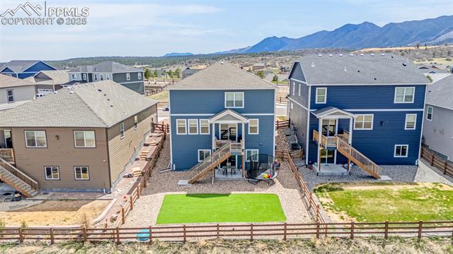 Rear of a blue two-story home with a raised deck, fenced yard, and mountain backdrop.