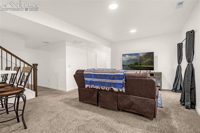 Living room with a brown sectional, blue patterned blanket, carpet, and staircase.