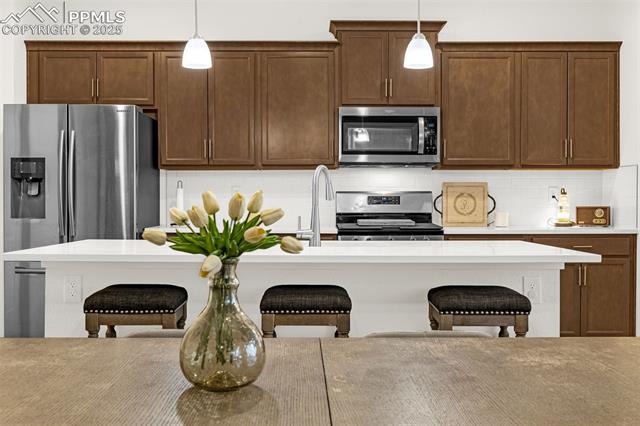 Kitchen with dark wood cabinets, stainless steel appliances, a white island, and three stools.