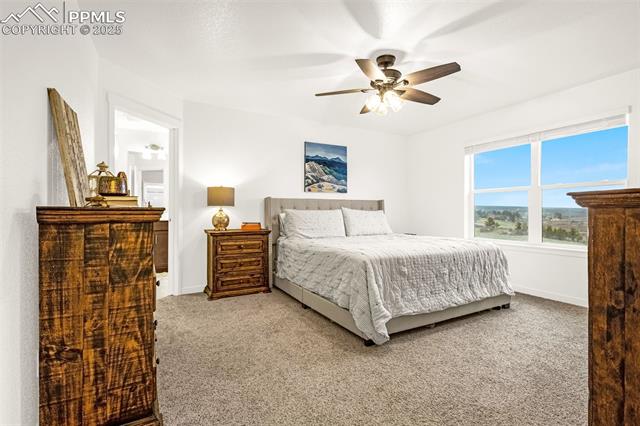 Staged bedroom with a king-size bed, wooden dressers, ceiling fan, and large landscape-view window.