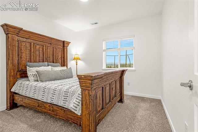 Bedroom with a carved wooden bed, patterned bedding, beige carpet, and a window.