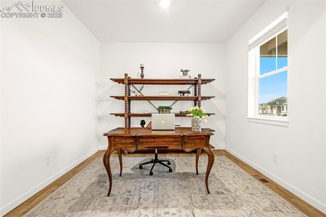 Furnished home office with a carved wooden desk, matching shelves, and a window overlooking neighboring homes.