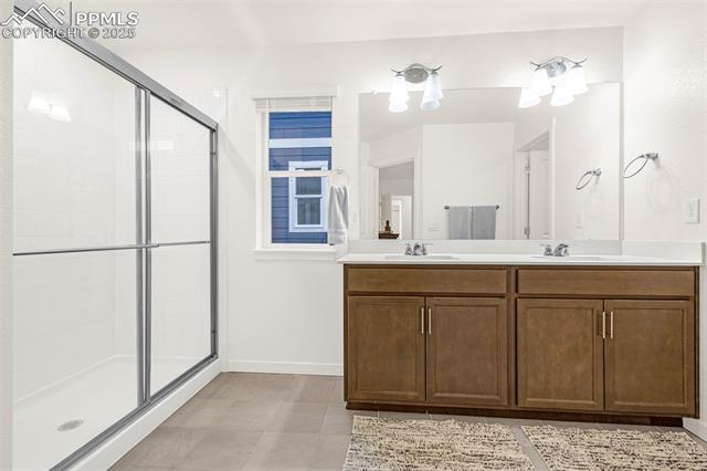 Bathroom with glass shower and double-sink vanity with brown wood cabinets.