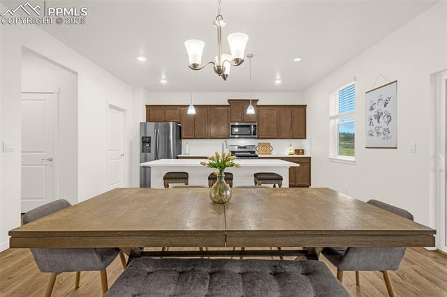 Dining table and chairs facing a kitchen with dark wood cabinets and stainless steel appliances.