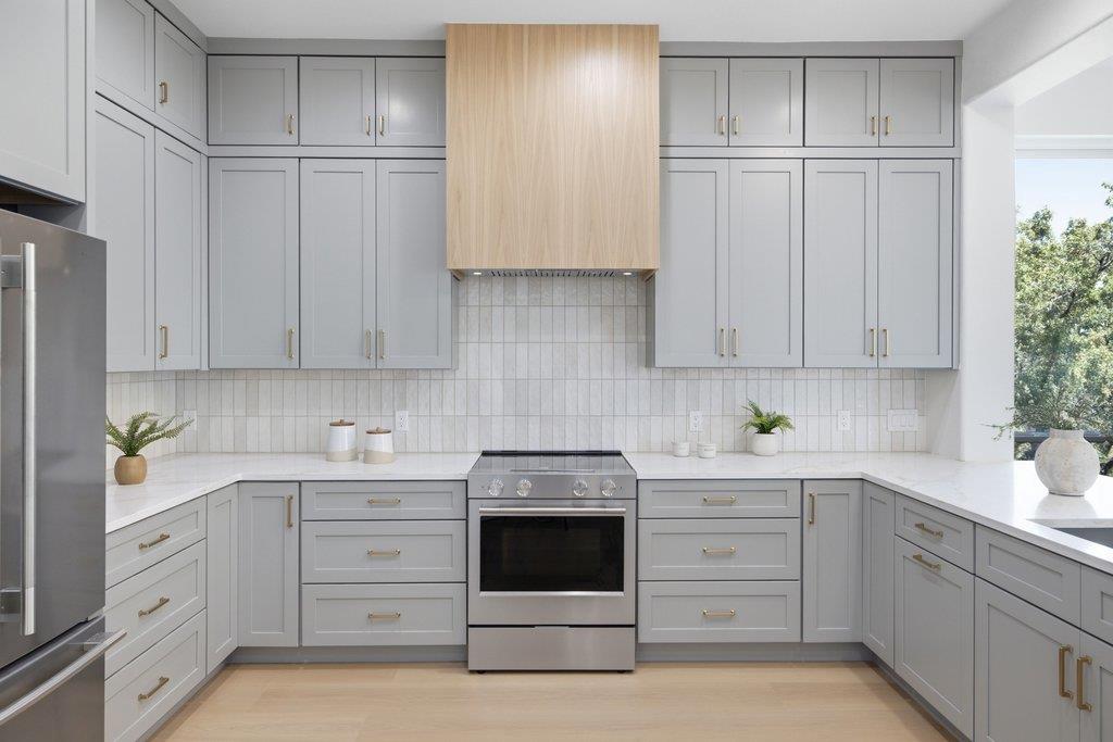 Kitchen with gray shaker cabinets, white counters, and a stainless steel range beneath a light wood hood.