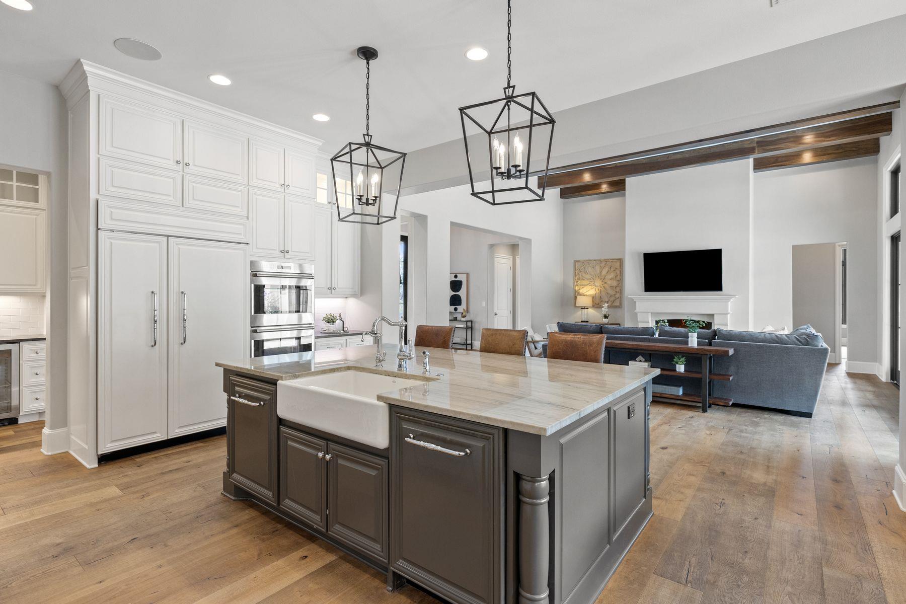 Open kitchen and living room with a large farmhouse-sink island, white cabinets, and exposed wood beams.
