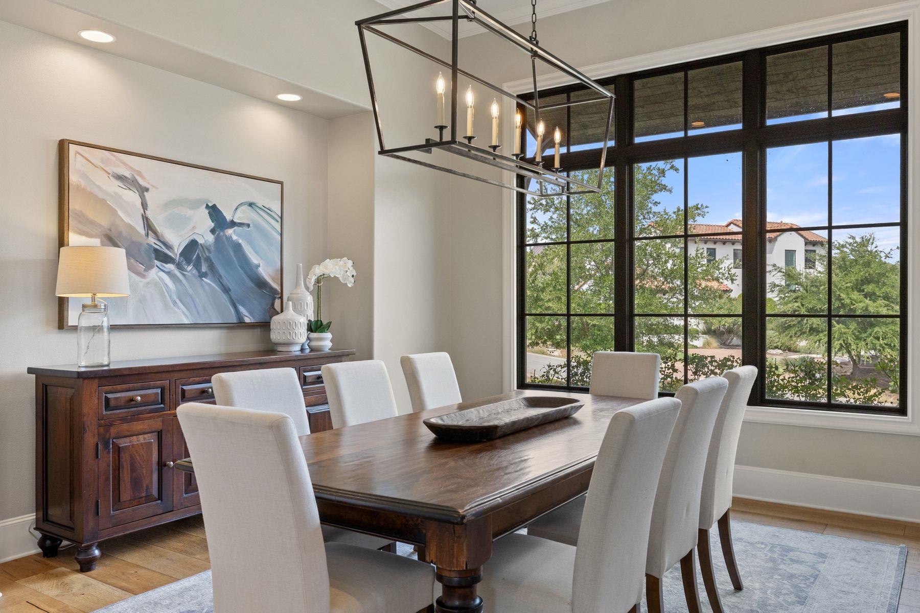Dining room with a dark wood table, upholstered chairs, and tall black-framed windows.