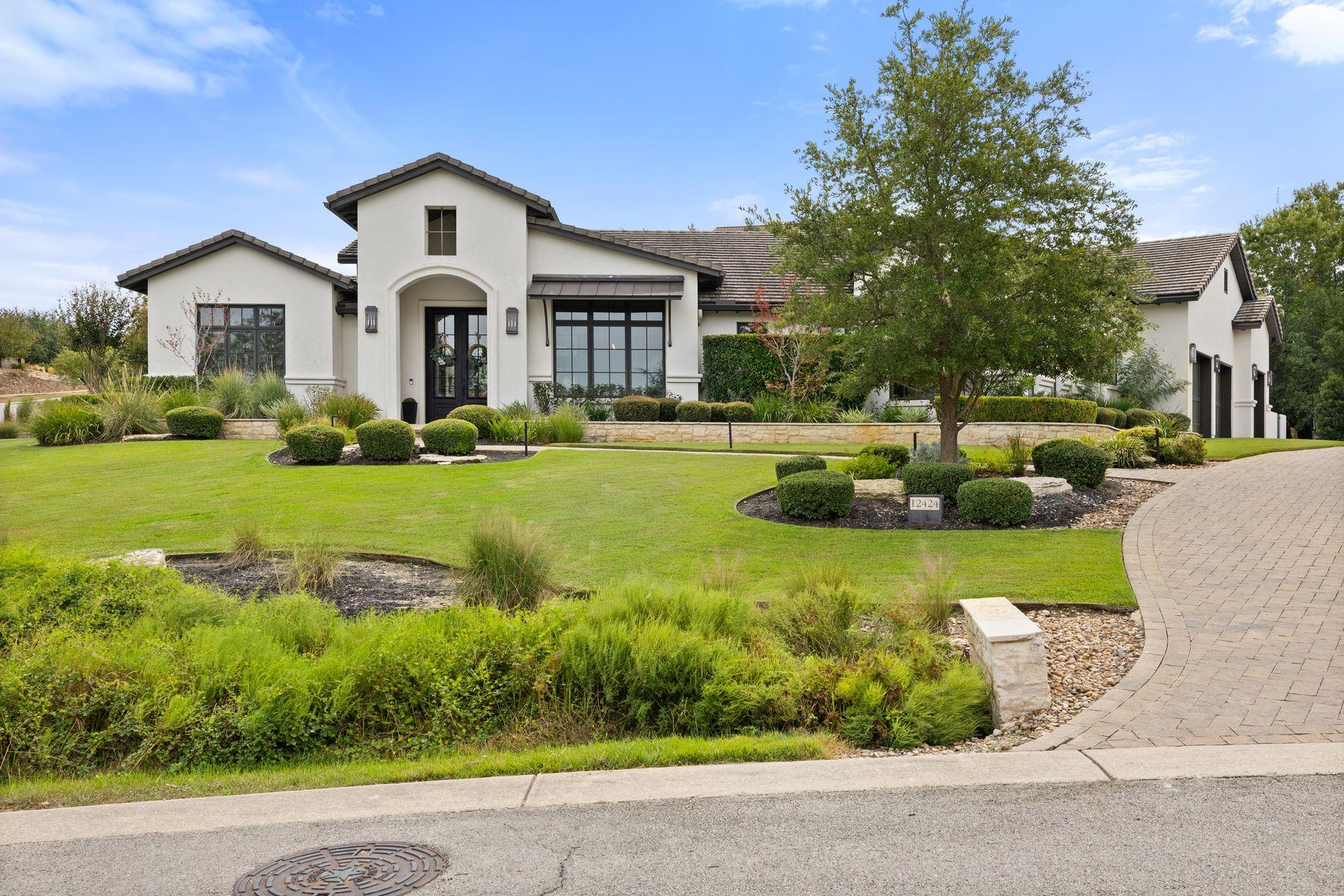 White stucco home with a tile roof, landscaped lawn, mature tree, and curved driveway.