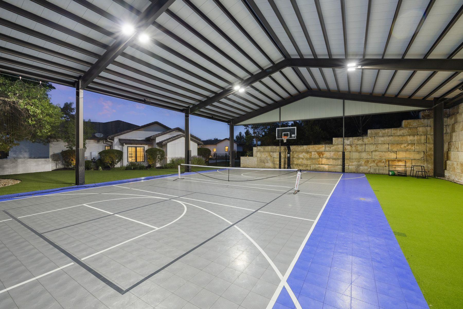 Covered outdoor court with basketball hoop, pickleball net, and green turf borders.