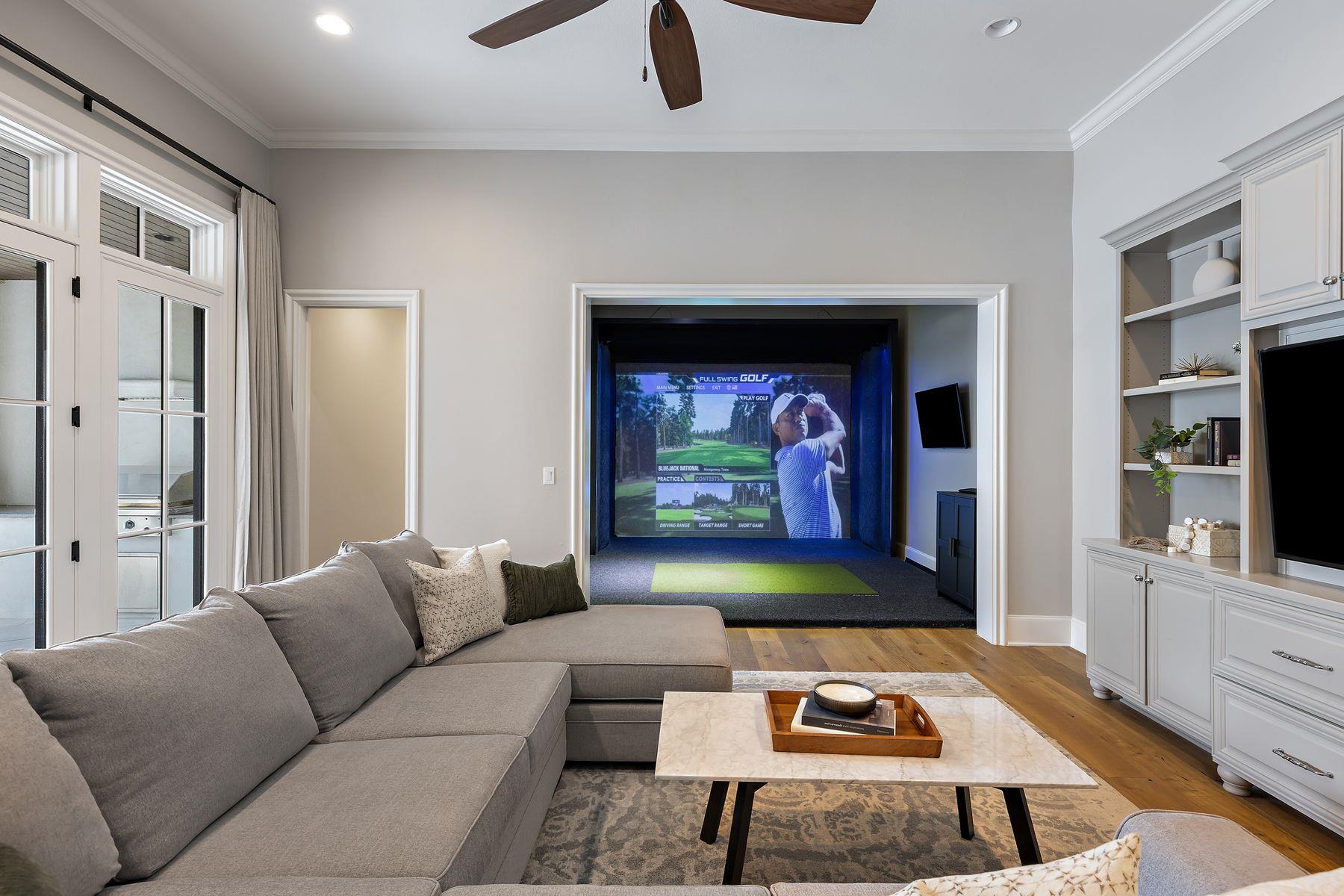 Living room with a gray sectional opening onto an indoor golf simulator.